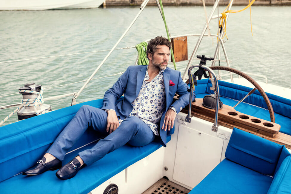 A man in a suit lounging on a boat with water in the background
