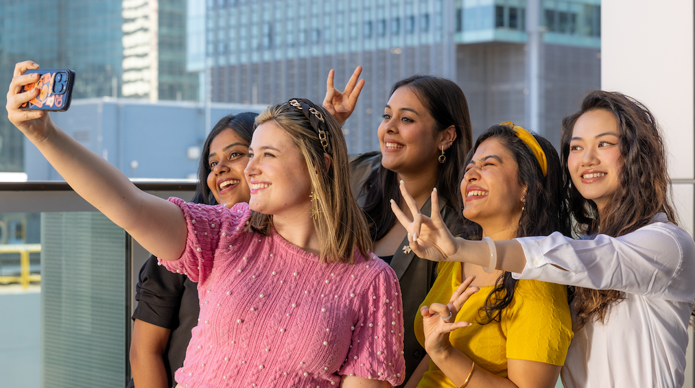 Five entrepreneurs smiling together while taking a group selfie for social media.